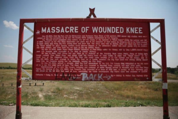 “Land Back” is spray painted on the bottom of a sign explaining the historical significance of the Wounded Knee Massacre on the Pine Ridge Reservation on July 30, 2024.