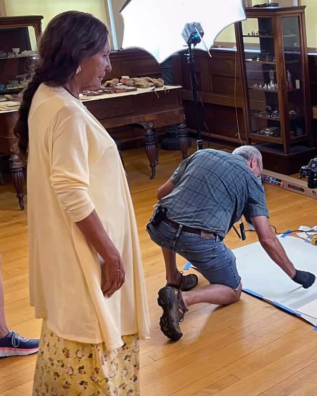 FILE - Leola One Feather, left, of the Oglala Sioux Tribe in South Dakota, observes as John Willis photographs Native American artifacts on July 19, 2022, at the Founders Museum in Barre, Mass. Federal penalties have increased under a newly signed law Wednesday, Dec. 21, 2022, intended to protect the cultural patrimony of Native American tribes. (AP Photo/Philip Marcelo, File)