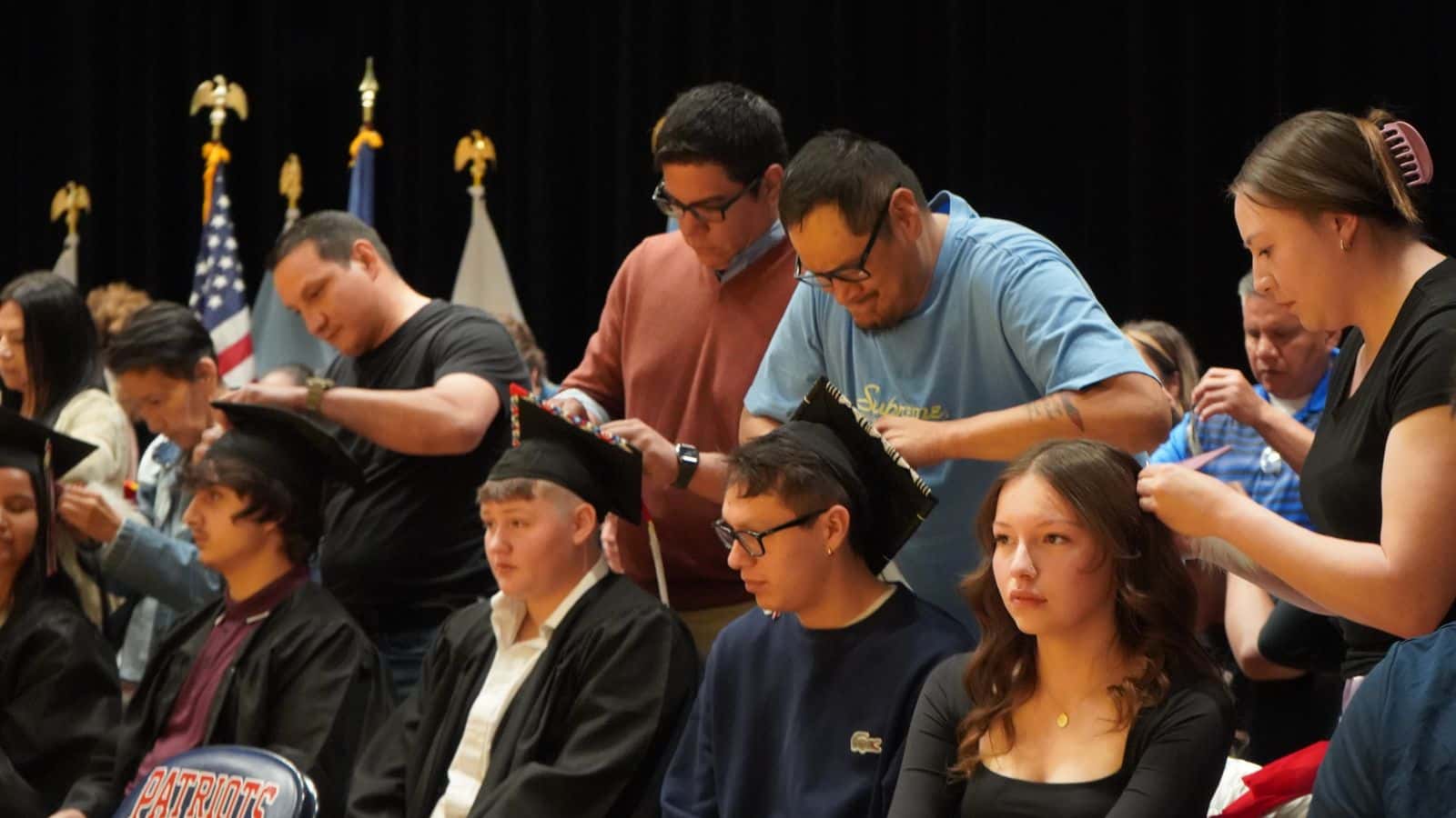 Mandan High School seniors Katawna Bailey, Marle Baker, Jerzi Brugh (right to left) sit as family members tie feathers into hair and onto graduation caps on May 15. Blair Baker ties a good knot on his son Marle's mortarboard.(Photo Credit, Jodi Rave Spotted Bear)
