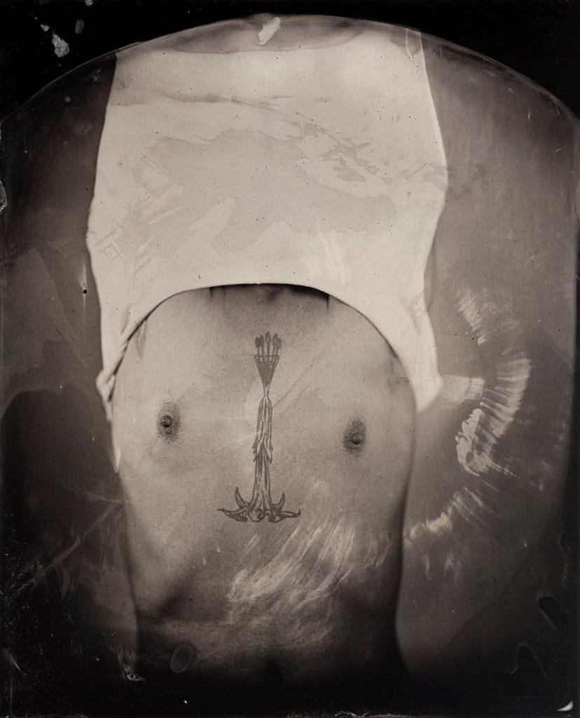 Kali Spitzer grey portrait first nations indigenous man taking off shirt revealing chest tattoo