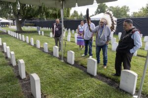 A group of Oglala Sioux gather by the grave of James Cornman (at lower left) at the Carlisle Barracks Post Cemetery in Pennsylvania. Three Oglala students who died at Carlisle - Fannie Charging Shield , Samuel Flying Horse, and James Cornman - were among 11 Native youths disinterred from the Carlisle cemetery starting Sept. 6, 2024, to be repatriated to their homelands. Pictured are, from left, Justin Pourier, Anna Diaz, Steve Durbay Jr., Steve Durbay Sr., and Jerome LeBeaux. (Photo by Charles Fox, special to ICT)